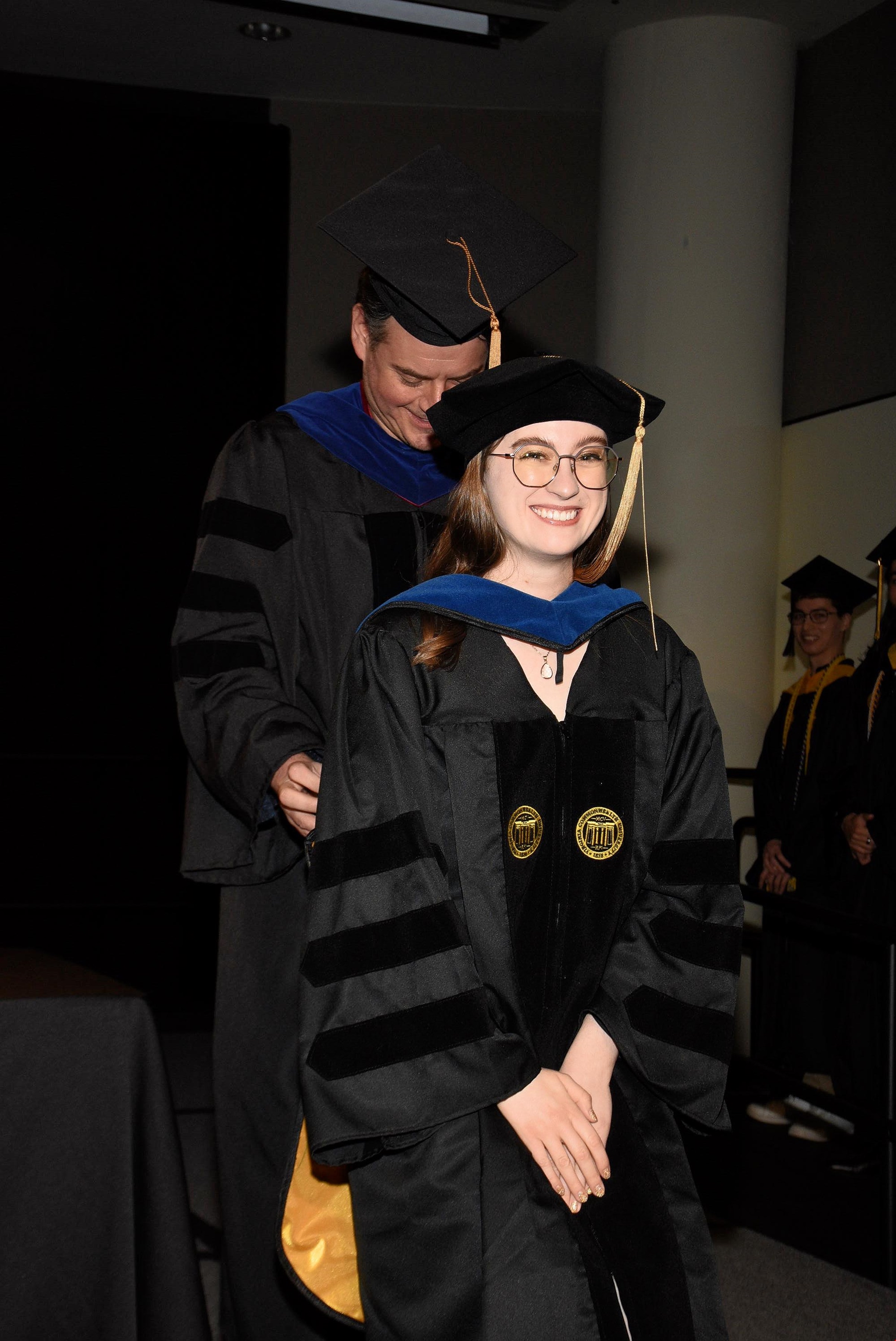 Morgan Holt Jackson, in graduation regalia, getting her sash adjusted by a man also in regalia